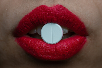A pill between female lips with bright red lipstick