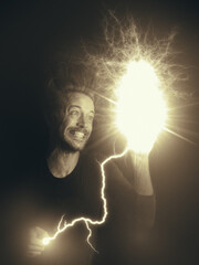 Sepia portrait of a young man having an idea holding a lightbulb in his hand which is being illuminated by a lightning strike. 