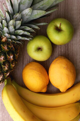 Pineapple, bananas, apples an dlemons on wooden background. Top view.