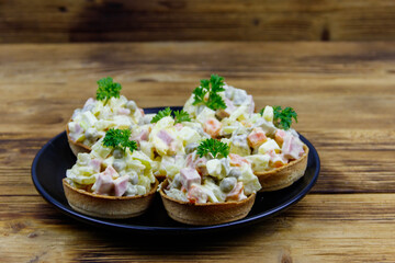 Traditional Russian festive salad Olivier in tartlets on wooden table