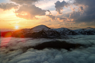 Aerial view of vibrant sunrise over white dense fog with distant dark Carpathian mountains on horizon.