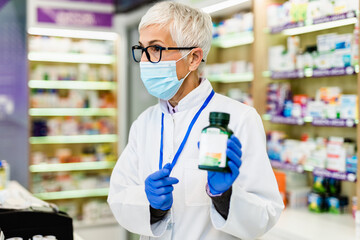 Senior female pharmacist with protective mask on her face working at pharmacy. Medical healthcare, Coronavirus, Covid-19 concept.