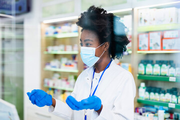 Black female pharmacist with protective mask on her face working at pharmacy. Medical healthcare, Coronavirus, Covid-19 concept.