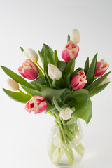 Bouquet of multi-colored tulips in a glass vase on a white background.
