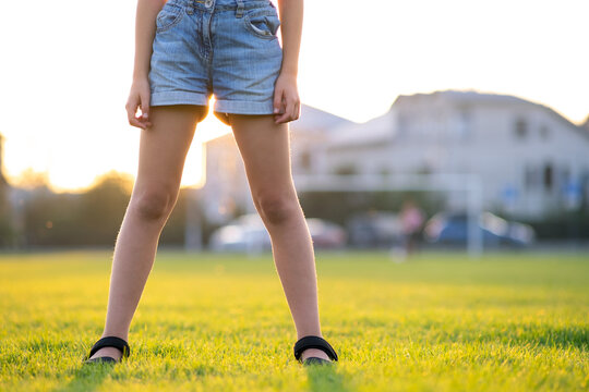 Closeup of young child girl legs in denim shorts standing on green grass lawn on warm summer evening.