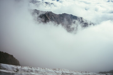 Wonderful mountain scenery with great rocks in dense low clouds. Atmospheric mountain landscape with big rocky mountains above clouds. Beautiful view from snowy top to high rocks over thick clouds.