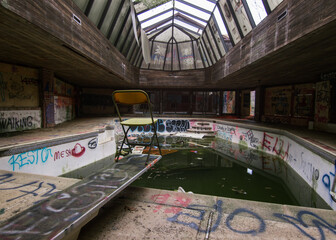 Empty chair looks out over abandoned swimming pool.