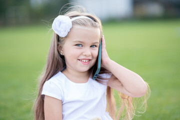 Pretty little child girl talking on mobile phone smiling happily outdoors in summer.