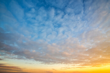 Dramatic sunset landscape with puffy clouds lit by orange setting sun and blue sky.