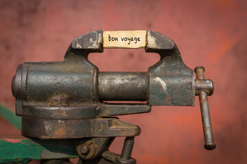 Vice grip tool squeezing a plank with the word bon voyage