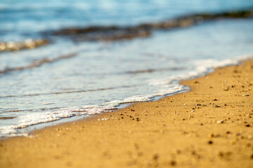 Fototapeta na wymiar Close up of small sea waves with clear blue water over yellow sand beach at summer sunny shore.