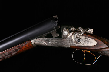 Details of an elegant double-barreled hunting classic shotgun on a black background close-up finished with a pattern for metal and carving on a wooden butt. Macro photography