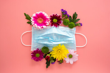 Medical blue face protective mask with colorful flowers on pink background. Creative concept of seasonal allergies. Spring 2021 concept.