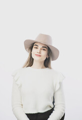 girl in a white sweater posing in a felt hat on a light background