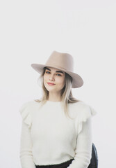 girl in a white sweater posing in a felt hat on a light background