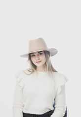 girl in a white sweater posing in a felt hat on a light background