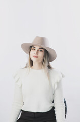 girl in a white sweater posing in a felt hat on a light background