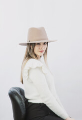 girl in a white sweater posing in a felt hat on a light background