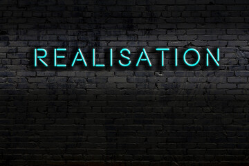 Night view of neon sign on brick wall with inscription realisation