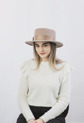 girl in a white sweater posing in a felt hat on a light background