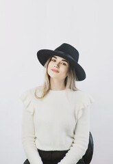 girl in a white sweater posing in a felt hat on a light background