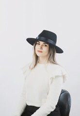 girl in a white sweater posing in a felt hat on a light background