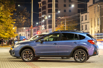 Obraz na płótnie Canvas Blue car parked on brightly illuminated city street at night.