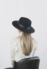 girl in a white sweater posing in a felt hat on a light background