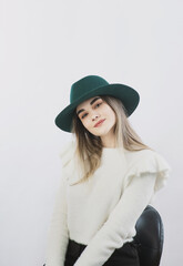 girl in a white sweater posing in a felt hat on a light background