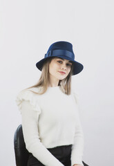 girl in a white sweater posing in a felt hat on a light background