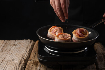 Cooking steak, chops with beef bacon on a grill pan by hands of a chef on a black background for copy space text restaurant menu