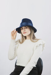 girl in a white sweater posing in a felt hat on a light background