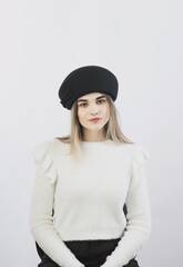 girl in a white sweater posing in a felt hat on a light background