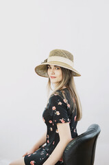 girl in a sundress and straw hat posing on a light, solid background