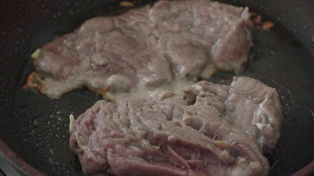 frying tenderloin steaks in a red skillet, on an aluminum stove. Meat still raw, start of preparation. Saut&eacute;ed in olive oil and garlic.