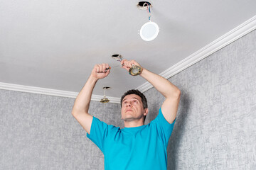 Middle-aged caucasian electrician removes old, inefficient halogen lamps from the ceiling and...