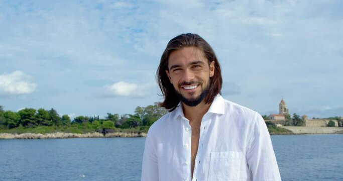 Man with brown long hair smiles at us on a boat with an island in the background - cinematic scene in slow motion with RED Camera 4K 