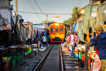 Naklejka premium Train on Tracks Moving Slow. Umbrella Fresh Market on the Railroad Track, Mae Klong Train Station, Bangkok, Thailand on a Sunny Day.