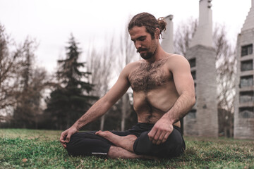 Fototapeta na wymiar Young man stretching and relaxing on a yoga session in the park. Breathing technique, healthy, fitness, contact with nature and wellness
