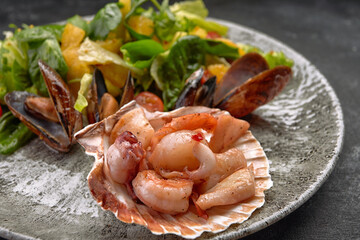 Seafood salad with pineapple and oranges on a plate, on a dark background