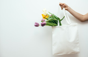 Female hand is holding eco bag with tulips on white background. Template for print. Spring shopping.