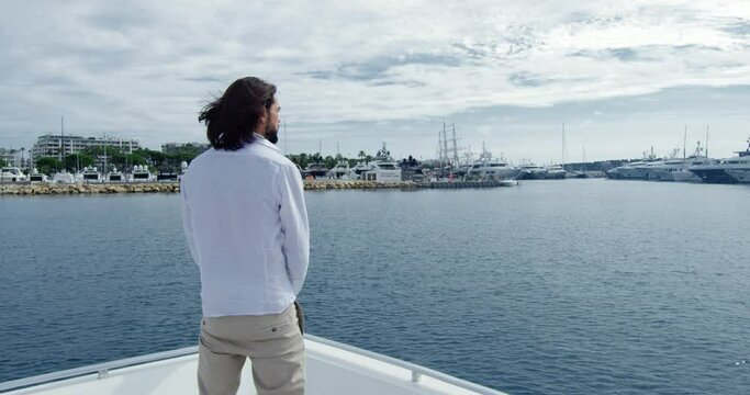 Handsome man from behind with brown hair standing on a boat sailing into the seagate - Cinematic scene with RED Camera 4K