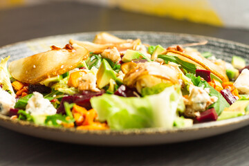 Clay plate with vegetable salad of caramelized pear, beetroot, arugula, avocado, carrot with dorblu cheese