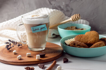Coffee latte cup with Love you sticker on wooden tray with turquoise bowls with cookies on gray wall background