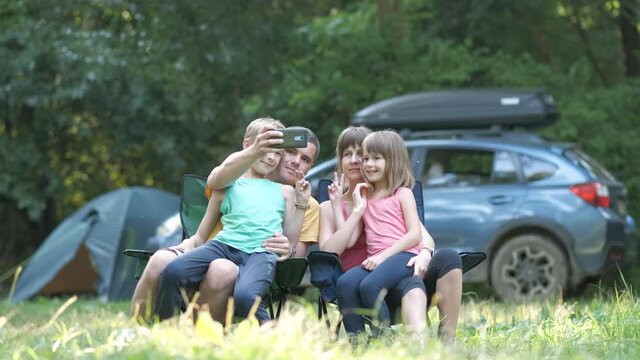 Happy family sitting together at campsite and taking selfie with mobile phone.