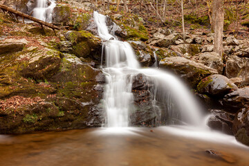 Long exposure image of the Dark Hallow Falls in Shenandoah National Park in autumn. Image features cascading water coming down the mountain covered with mossy rocks and trees.