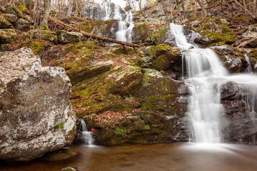 Fototapeta na wymiar Long exposure image of the Dark Hallow Falls in Shenandoah National Park in autumn. Image features cascading water coming down the mountain covered with mossy rocks and trees.