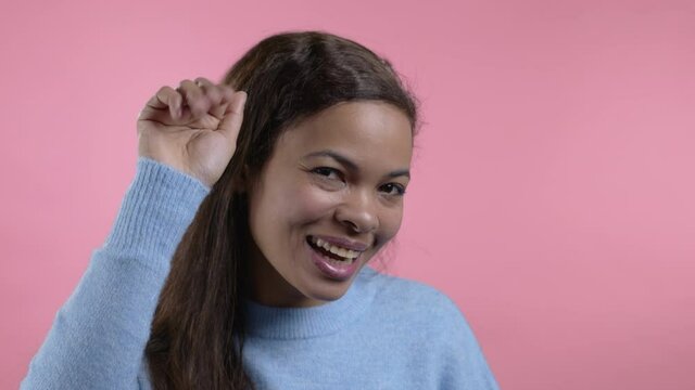 African friendly woman waving hand - goodbye, chao, adios. Parting, say bye to camera. Beautiful lady waving hand on pink studio background. 