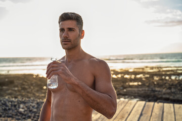 Handsome young man after outdoor workout drinking water. Athletic , muscular shirtless guy resting.