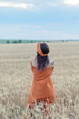 Pretty young girl in orange dress and headband on the field back view